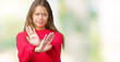 © Krakenimages.com - Young beautiful brunette woman wearing red winter sweater over isolated background Rejection expression crossing arms and palms doing negative sign, angry face