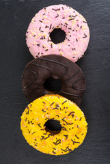 Canvas Print - Homemade donuts with colored icing on black background.