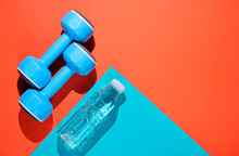 Minimalistic Sport Concept. Blue Plastic Dumbbells, Bottle Of Water On Colored Paper Background. Top View