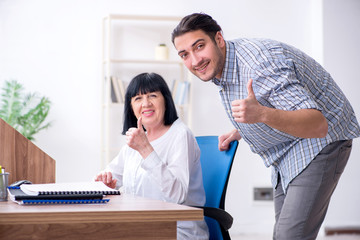 Young male employee explaining to old female colleague how to us