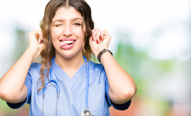 Poster - Young adult doctor woman wearing medical uniform Smiling pulling ears with fingers, funny gesture. Audition problem