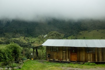 Sticker - Small wooden house built in a green beautiful hill with mist and fog above