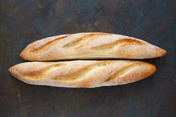 Two freshly baked baguettes on dark brown background. Top view.