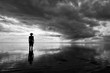 © lazyllama - Moody monochrome silhouette of man in hat standing in calm shallow waters reflecting dramatic skyscape on the sea horizon