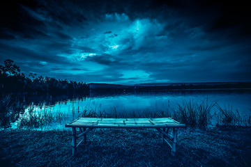 Wall Mural - bamboo litter on grass in front of lake and moonlight behind a cloudy at night time