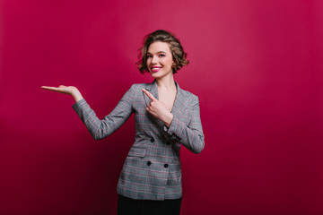 Wall Mural - amazing pleased curly woman in gray jacket posing in studio. laughing brunette girl isolated on clar