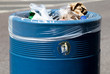 Overflowing blue metal public waste bin with plastic liner 