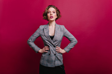 Wall Mural - Winsome business lady with short haircut posing in studio. Photo of confident girl in tweed jacket isolated on claret background.