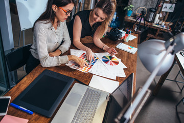 Wall Mural - two female architects working together using color swatches sitting at desk with laptop, graphic tab