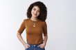 © Cookie Studio - How can help you. Gentle lovely curly hair charming young woman hold hands jeans pockets confident friendly smile tilting head listen customer interesting story listen, white background
