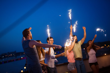 Wall Mural - Friends enjoying a rooftop party and dancing with sparklers