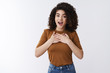 © Cookie Studio - Touched amazed surprised pretty curly dark hair girl speechless grateful hold hands chest gasping amused open mouth stare camera astonished receive gift thankfully gazing forward, white background