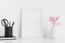 White Frame Mockup With Pink Oleander In A Glass Vase And Workspace Accessories On A White Table.Portrait Orientation.