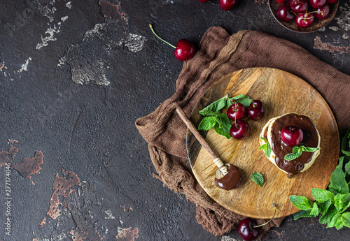 Fototapeta na szkło Stack of fluffy pancakes or fritters with chocolate and cherry jam, fresh cherry and mint. Delicious dessert for breakfast. Dark stone background, rustic style.