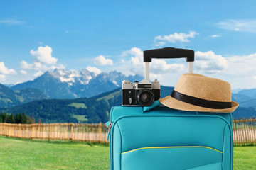 Wall Mural - recreation image of traveler luggage, camera and fedora hat infront of a rural lanscape. holiday and vacation concept