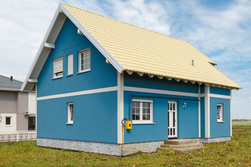 a small blue house with white windows and a light yellow metal roof.