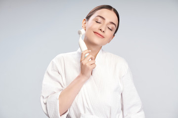 Wall Mural - Beautiful young woman in white bathrobe using pore cleansing brush