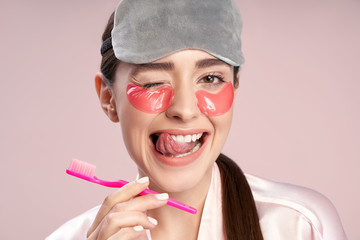 Wall Mural - Cheerful girl with under-eyes patches licking teeth with tongue and winking