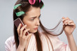 © Yakobchuk Olena - Upset girl with curlers in hair talking on cellphone and holding hair strand