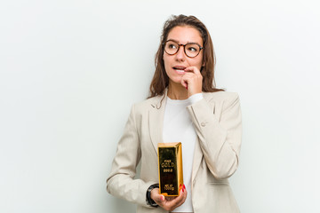 Wall Mural - Young european business woman holding a gold ingot relaxed thinking about something looking at a copy space.