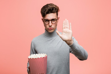 Wall Mural - Young intellectual man holding a popcorn bucket pointing his temple with finger, thinking, focused on a task.