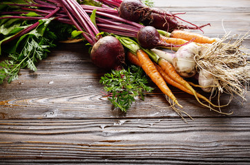 Fresh organic beetroots green garlic and carrots on kitchen wooden rustic table close up view