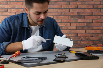 Canvas Print - Technician repairing broken smartphone at table in workshop