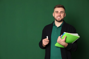 Wall Mural - Portrait of young teacher with notebooks and chalk on green background. Space for text