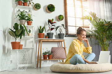 Young woman using laptop in room with different home plants