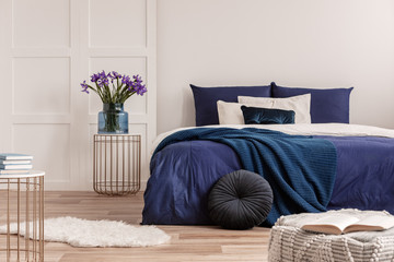 flowers in vase on bedside table next to king size bed with navy blue bedding