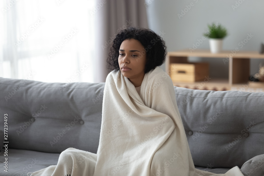 Sick african woman feeling cold covered with blanket at home - obrazy, fototapety, plakaty 