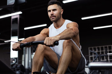 Fit and muscular man using rowing machine at gym.