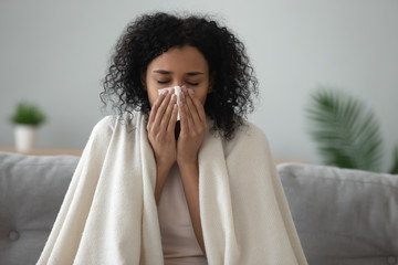 ill african woman covered with blanket blowing nose got flu