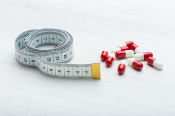 Wall Mural - Red and white diet pills lie on a white table next to a measuring tape. Concept of weight loss with the help of medicines.