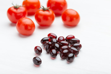 Wall Mural - Tomatoes lie on a white table next to vitamins in the form of jelly on a white table. Concept of vitamins and minerals.