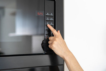 Woman holding hand on black microwave button