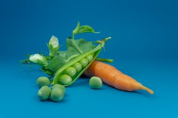 Pea pods carrot and peas on blue background