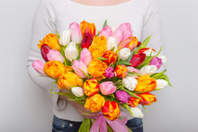 Very Nice Florist Woman Holding A Beautiful Colourful Blossoming Flower Bouquet Of Fresh Tulips Leaves On The White Wall Background.