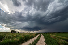 A Supercell Thunderstorm Looms In The Sky Over A Dirt Road In Farm Country.