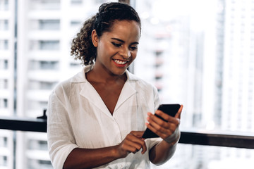 Smiling beautiful professional business african american black woman working and using smartphone standing in office