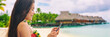 Happy Asian tourist using mobile phone texting sms message on travel holiday vacation panoramic banner of luxury hotel background.
