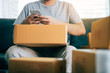 © wutzkoh - Asian young man using smart phone for checking shipment at home.