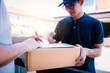 © wutzkoh - Delivery young man standing at the door of home and carrying parcels for young male to signing.