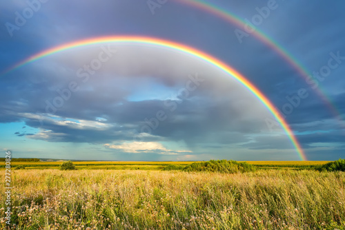 Rainbow over stormy sky. Rural landscape with rainbow over dark stormy sky in a countryside at summer day. © sborisov