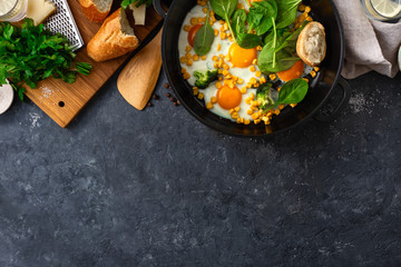 Canvas Print - Family breakfast table with fried eggs spinach and corn top view on dark stone background with copy space