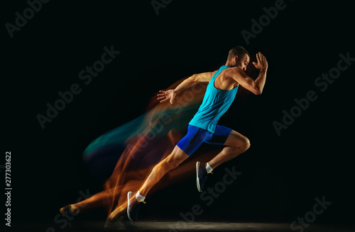 Fotomural Professional male runner training isolated on black studio background in mixed light