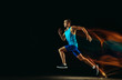 © master1305 - Professional male runner training isolated on black studio background in mixed light. Man in sportsuit practicing in run or jogging. Healthy lifestyle, sport, workout, motion and action concept.