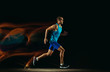 © master1305 - Professional male runner training isolated on black studio background in mixed light. Man in sportsuit practicing in run or jogging. Healthy lifestyle, sport, workout, motion and action concept.