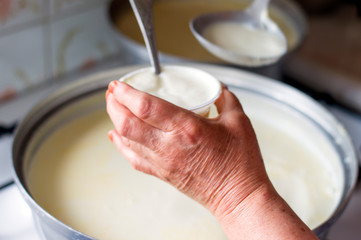 Hands of senior woman who is making homemade yoghurt ( yogurt ) with selective focus. Fermentation of yoghurt with blurred background. 