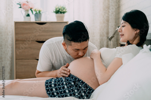 Pregnant Couple Hugging And Kissing At Home In Bedroom